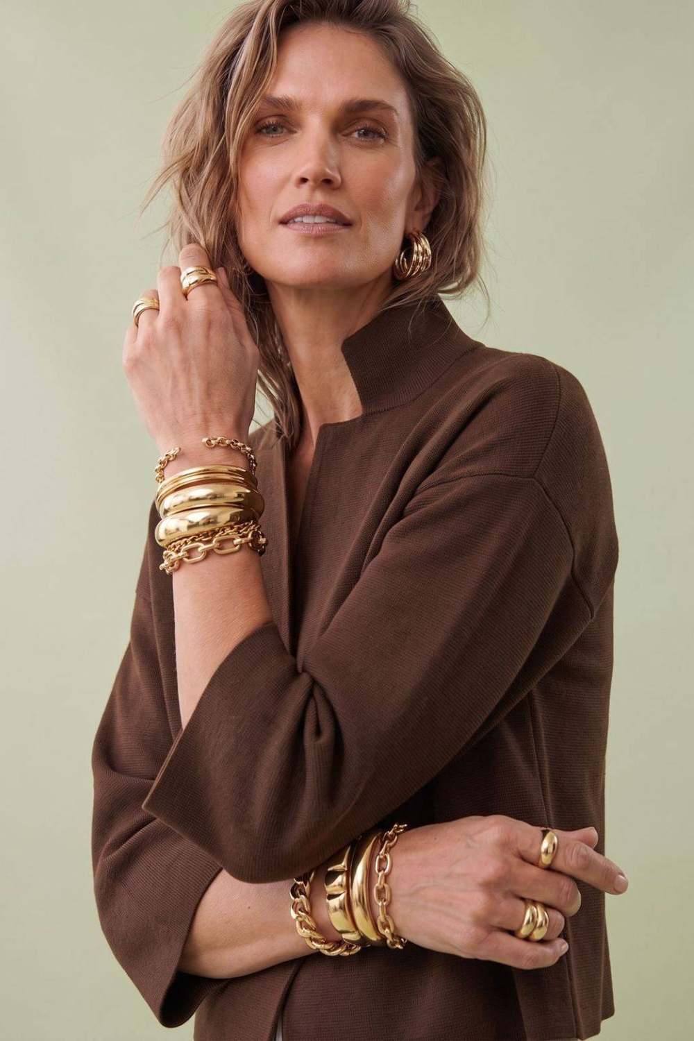 Close detail of a chocolate knit sleeve, stacked gold bracelets and rings